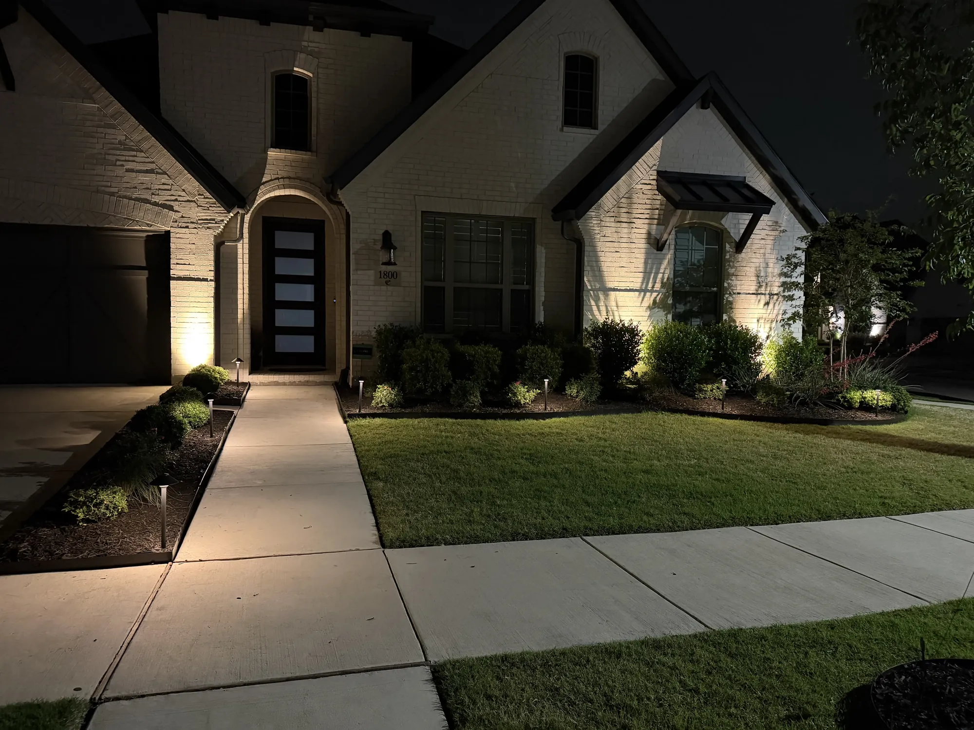 Landscape lighting illuminating a home and planting beds at night in Double Oak, TX