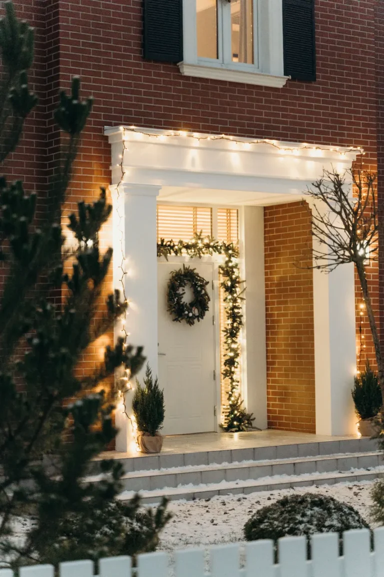 Warm white Christmas lights, garland and a wreath framing the front entry of a home at dusk