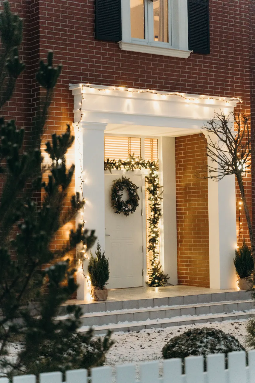 Warm white Christmas lights, garland and a wreath framing the front entry of a home at dusk
